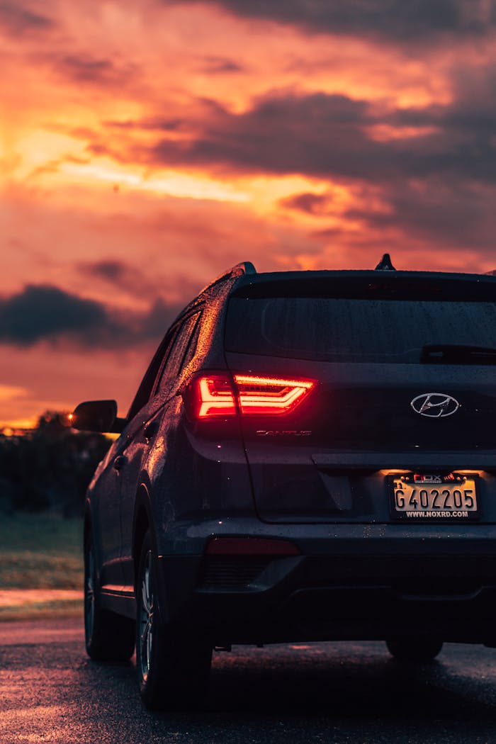 about-us-01 Rear view of a modern Hyundai SUV on a wet road during a vibrant sunset, showcasing dramatic cloudscape.
